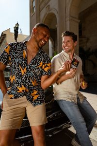 Men sharing cigarillos at sunset leaning against a car