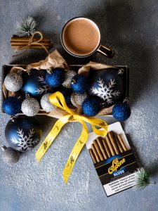 Holiday gift bags filled with wine, chocolates, candles, and Al Capone cigarillos on a festive table