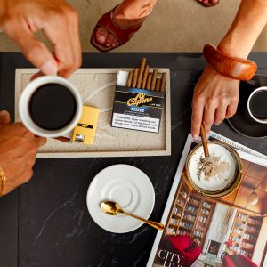 A cigar resting beside a classic cocktail on a bar