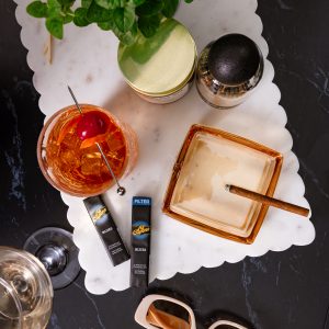 A cigar resting beside a classic cocktail on a bar